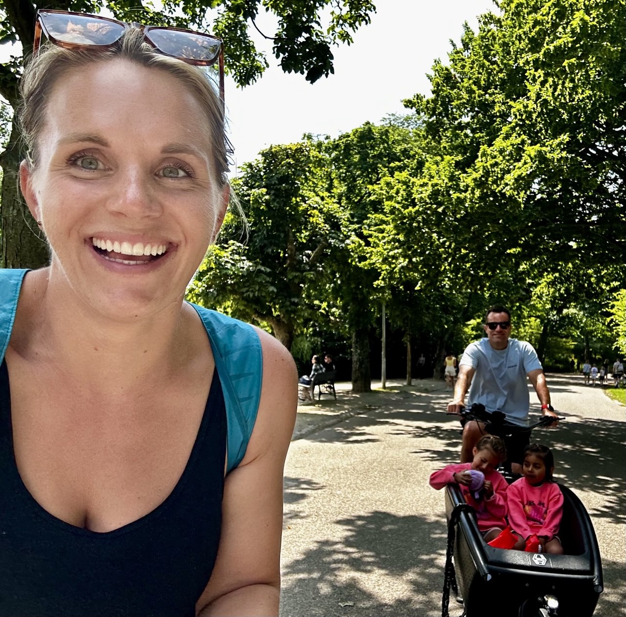 Michaela with her family on a sunny park path, the girls riding along on a cargo bike