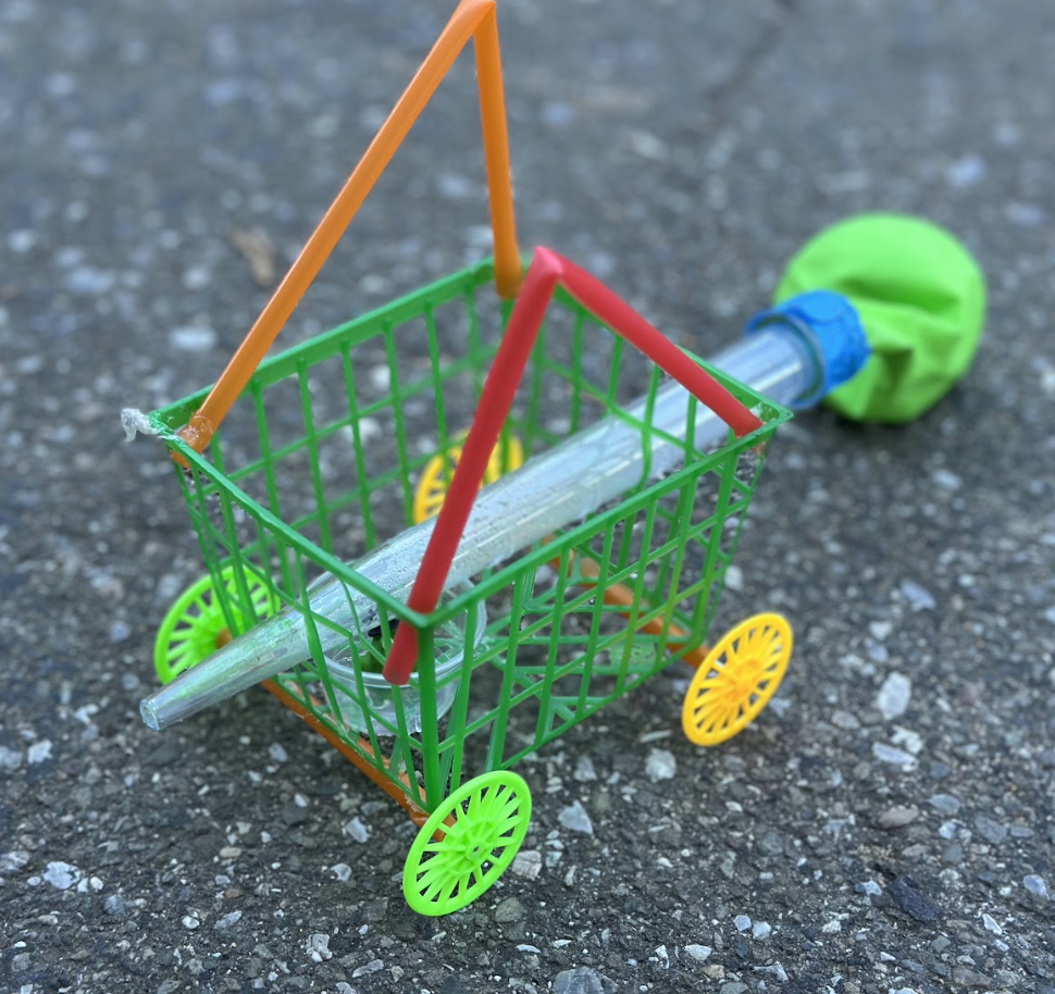 A balloon powered car built from a basket, straws, and wheels.